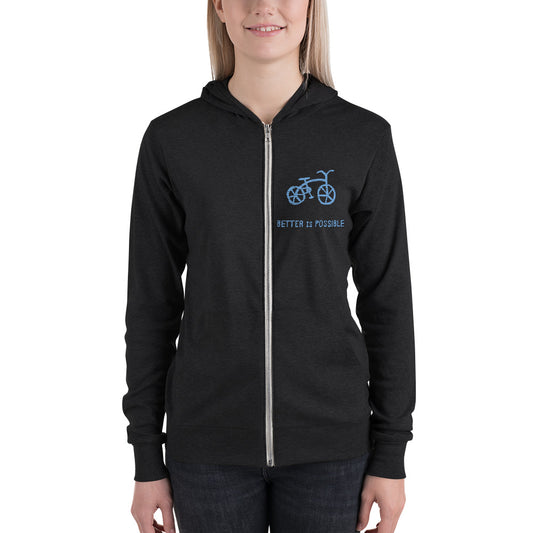 A woman wearing a black unisex zip hoodie with a front zipper and a kangaroo pocket. The hoodie has a blue graphic of a bicycle and the text 'Better is Possible' on the front.