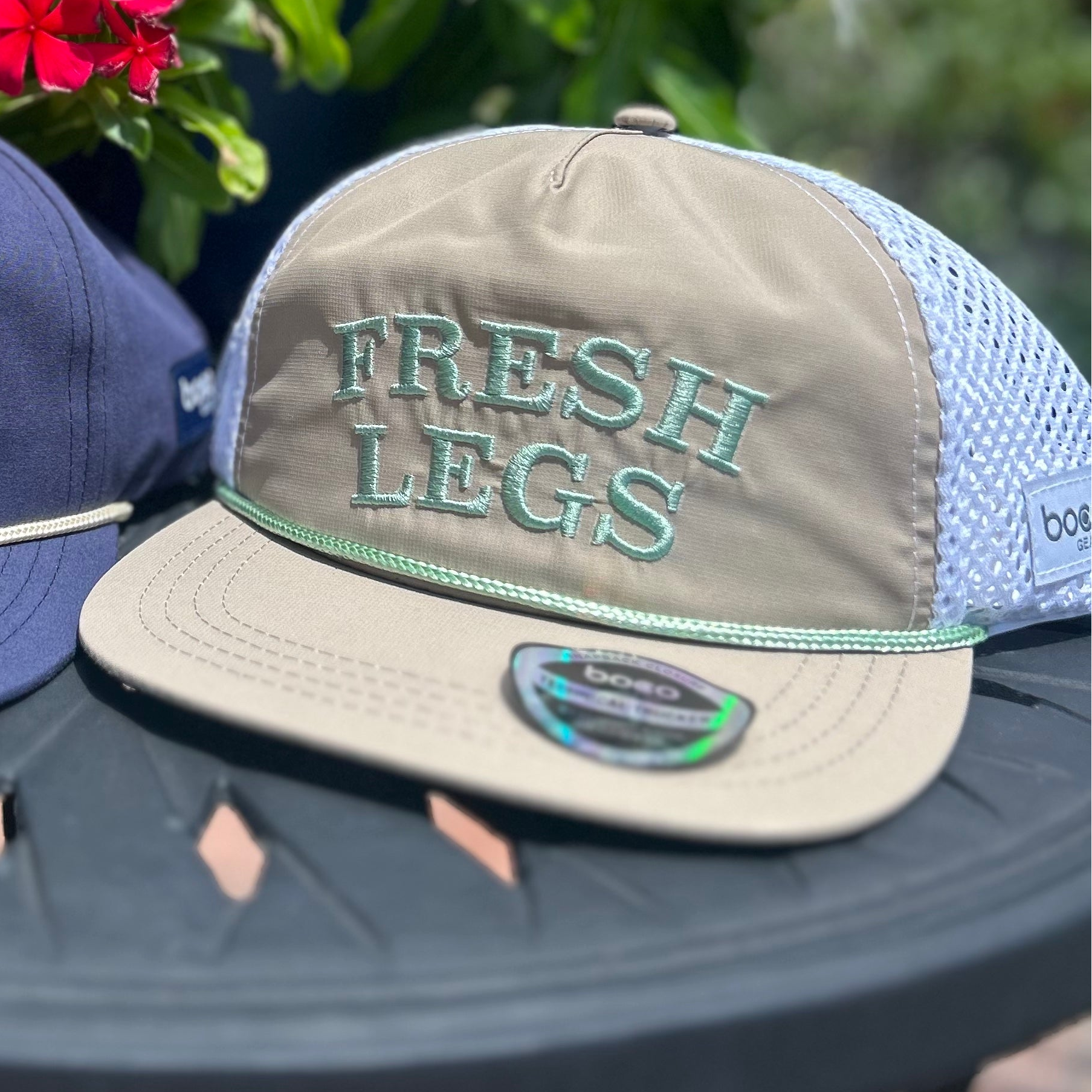 Two hats with text on a table outdoors with flowers in the background